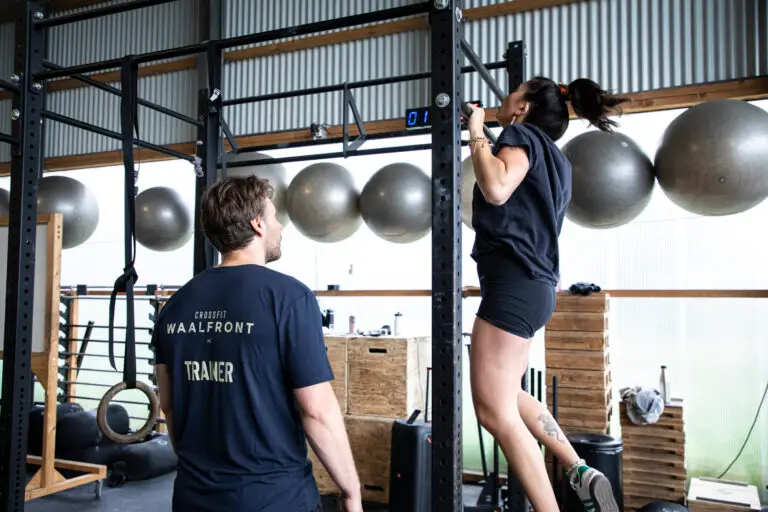 Trainer begeleidt een lid bij een pull-up aan de rig tijdens Gymnastics