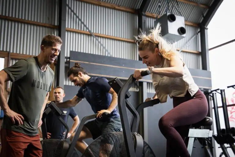 Leden trainen fanatiek op de assault bikes tijdens de WOD, aangemoedigd door een coach