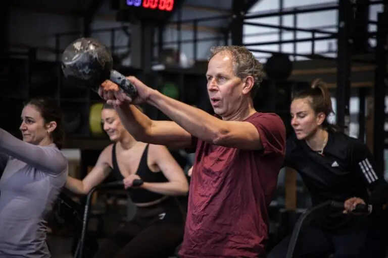 Lid maakt een kettlebell swing tijdens de WOD, met op de achtergrond leden op de bikes